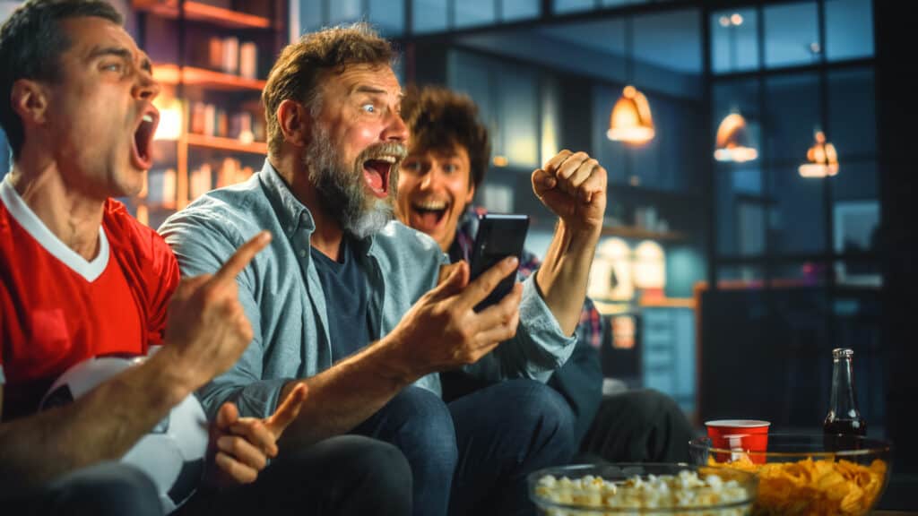 Three Soccer Fans Sitting on a Couch Watch Game